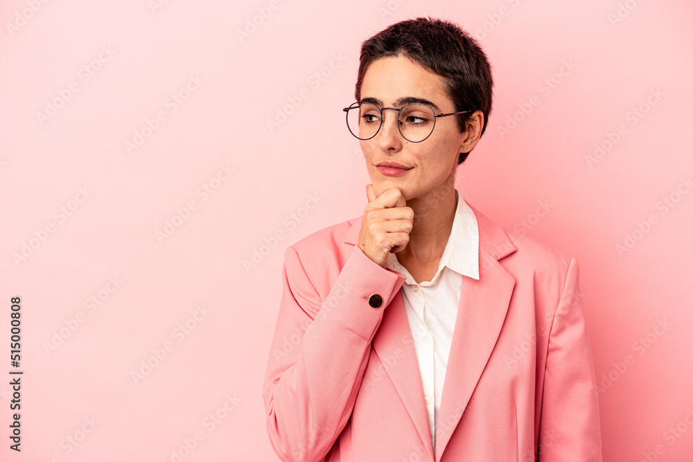 Young business woman wearing a pink blazer isolated on pink background looking sideways with doubtful and skeptical expression. Young business woman wearing a pink blazer isolated on pink background looking sideways with doubtful and skeptical expression.
