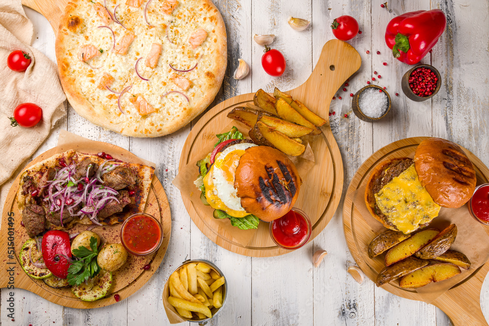 Burger with egg and beef patty, salmon pizza and skewers of lamb on white wooden table top view Burger with egg and beef patty, salmon pizza and skewers of lamb on white wooden table top view
