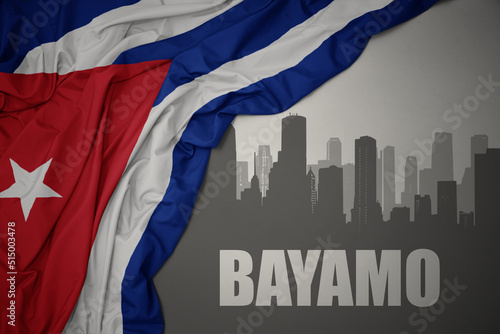 Photography abstract silhouette of the city with text Bayamo near waving national flag of cuba on a gray background