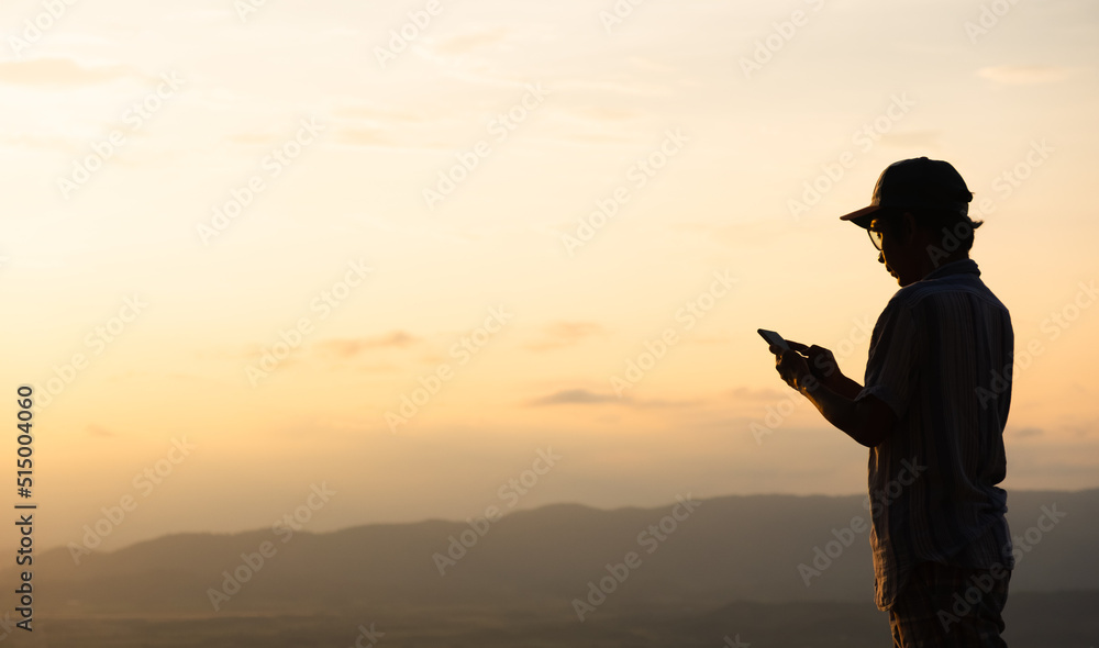The man in the hat is standing with his phone facing the sunset.copy space