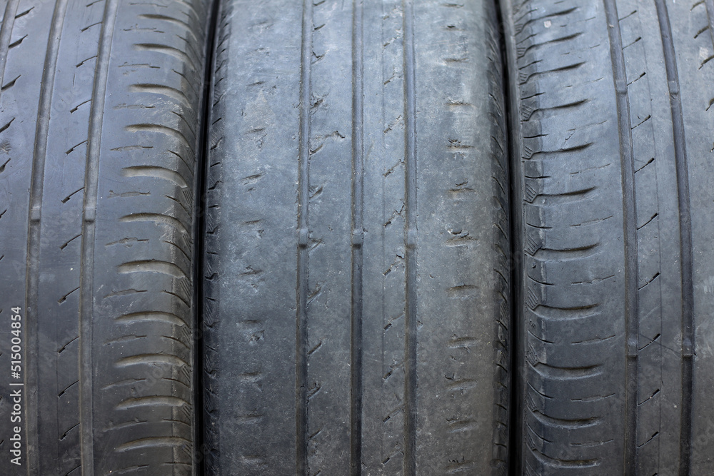 Fototapeta premium Old summer tire next to another old summer tire and worn tire next to smooth old tire close-up