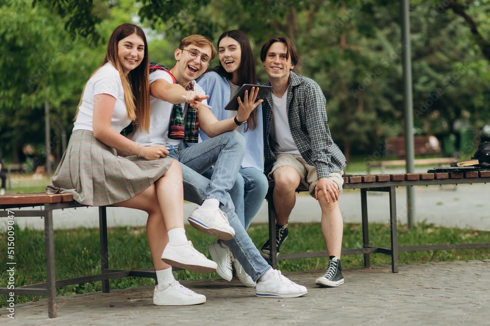 Group of four cheerful friends, students spending time together at the park, relax after lesson Group of four cheerful friends, students spending time together at the park, relax after lesson