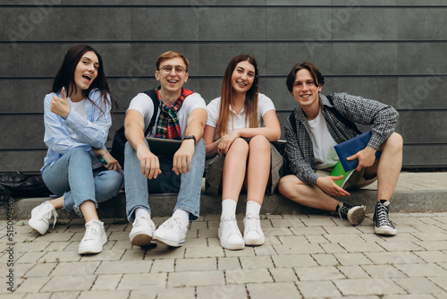 Group of happy smiling students sitting on the floor against dark wall. College learning concept