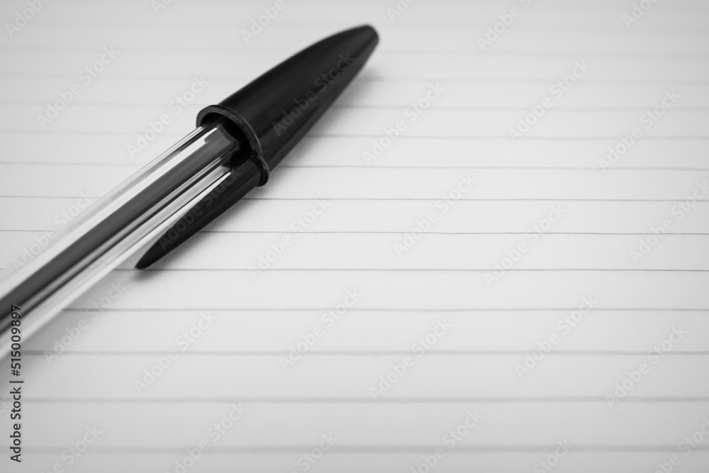 Close-up of a black pen resting on a lined paper sheet. Macro shot with selective focus and empty space for text Close-up of a black pen resting on a lined paper sheet. Macro shot with selective focus and empty space for text