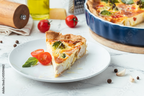 Quiche with chicken decorated with tomatoes, basil and broccoli. French pie with shortcrust pastry base on the white marble background