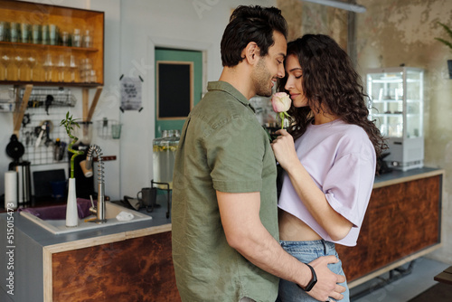 Fotografi Young affectionate man standing close to his gorgeous girlfriend smelling pink r