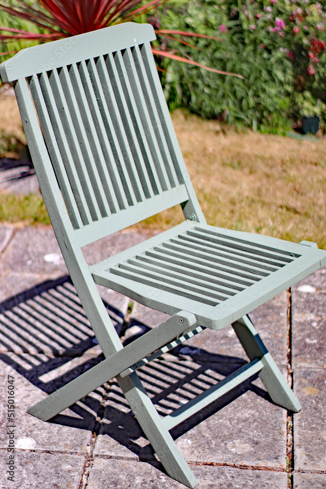 An old green folding wooden chair on a patio in an English garden An old green folding wooden chair on a patio in an English garden