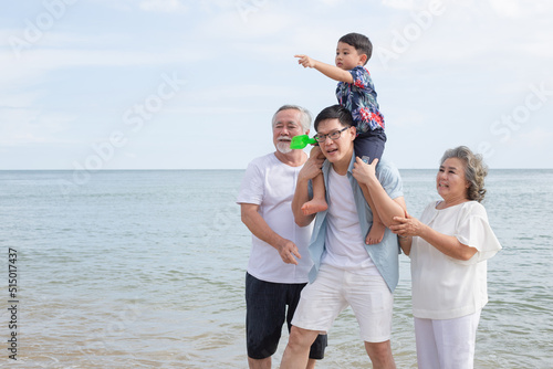 Asian family walking on the beach together. son sitting on father's shoulder with support from grandmother and grandfather. travel vacation on summer