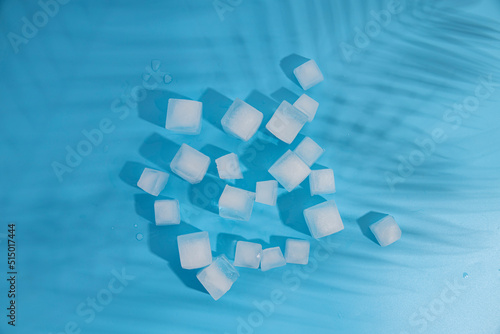 Many ice cubes under the shadow of palm leaves on a blue background
