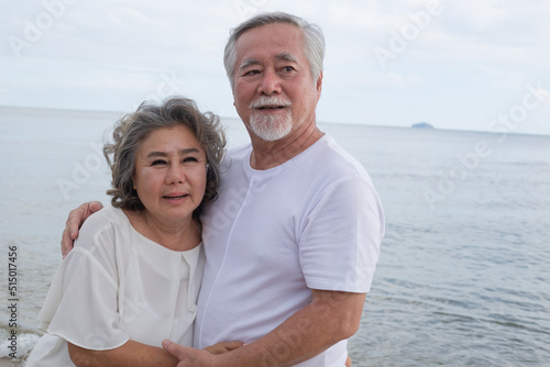 Portrait of happy Asian senior couple embracing together and smiling. retired people relaxing on holiday at the beach in summer weather. healthy people with happiness lifestyle for insurance concept
