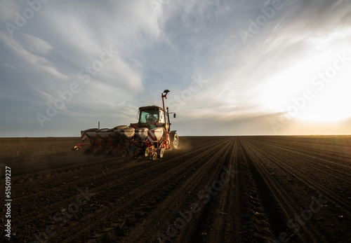 Farmer with tractor seeding - sowing crops at agricultural field