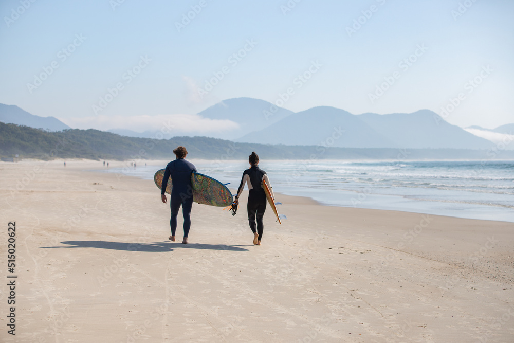 surfer couple walking on the beach