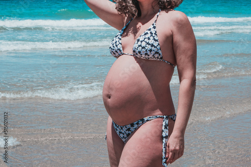 Pregnant woman on the beach. Adult lady on the beach about to give birth. High risk pregnancy. Miss shows the belly of her 8-month-old unborn baby.