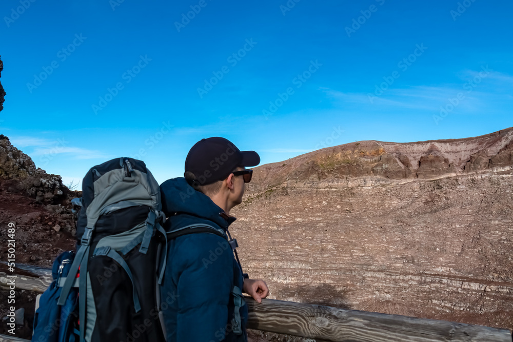 Happy tourist man with big backpack at the edge of active volcano crater of Mount Vesuvius, Province of Naples, Campania, Italy, Europe, EU. Person enjoying the view on the mountain summit. Awe Happy tourist man with big backpack at the edge of active volcano crater of Mount Vesuvius, Province of Naples, Campania, Italy, Europe, EU. Person enjoying the view on the mountain summit. Awe