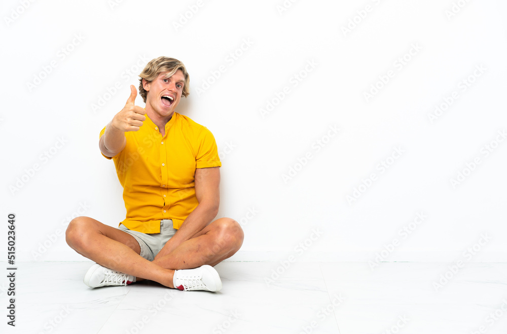 Fototapeta premium Young English man sitting on the floor with thumbs up because something good has happened