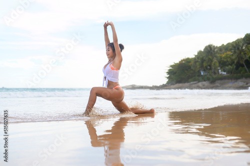 Young asian woman in bikini doing yoga on the beach, health and meditation concept