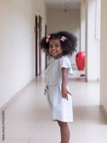 Portrait of cute little African girl with Afro hair style posing and looking at camera while walking in a walkway