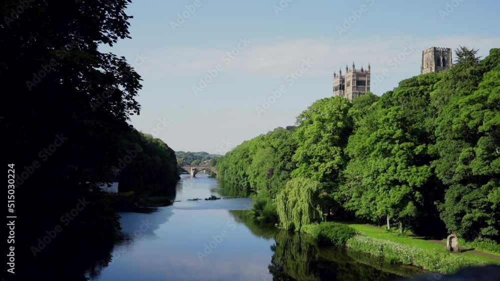 Durham England: 2022-06-07: Durham Cathedral view from the riverside (River Wear) with green trees lining the water during sunny summer day Durham England: 2022-06-07: Durham Cathedral view from the riverside (River Wear) with green trees lining the water during sunny summer day