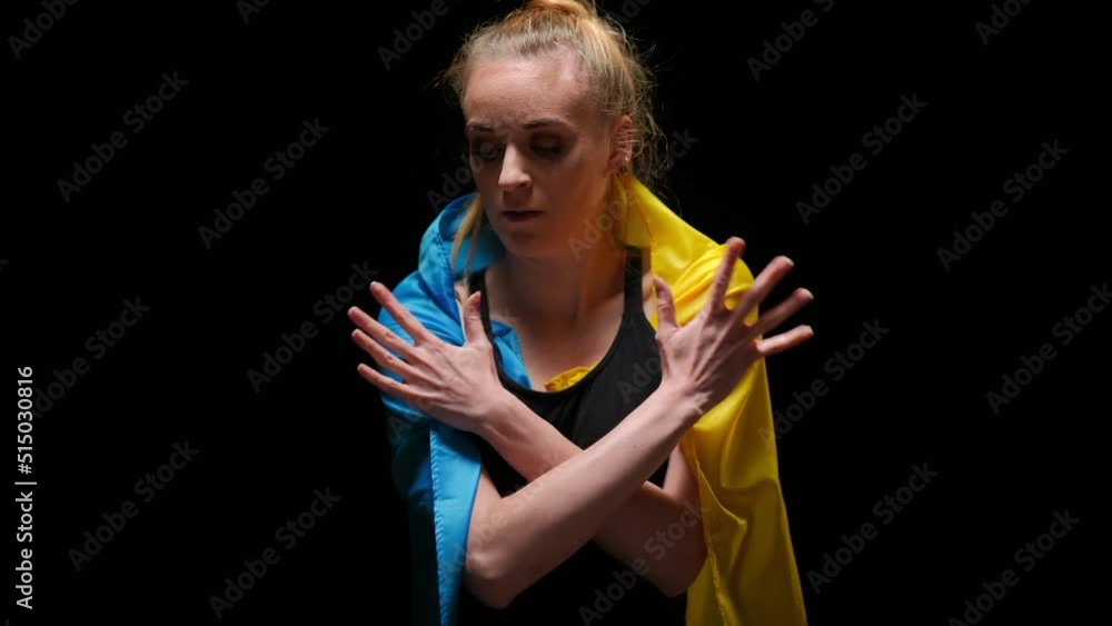 Woman in Ukrainian flag walking from darkness looking at camera with hoping facial expression. Beautiful young lady posing at black background medium shot. Hope and war concept Woman in Ukrainian flag walking from darkness looking at camera with hoping facial expression. Beautiful young lady posing at black background medium shot. Hope and war concept