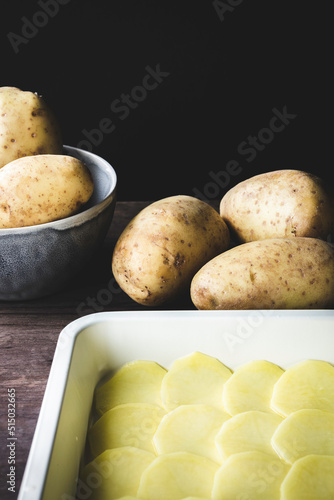 patatas crudas enteras y patatas cortadas en rodajas en una bandeja para hornear photo