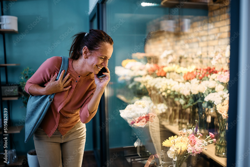 Happy woman talking on the phone while looking at flowers in floral cooler at flower shop. Happy woman talking on the phone while looking at flowers in floral cooler at flower shop.