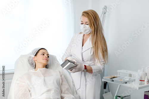 Experienced female cosmetologist gives consultation to a young female patient lying on a sofa in a cosmetologist s office of an aesthetic clinic. High quality photo