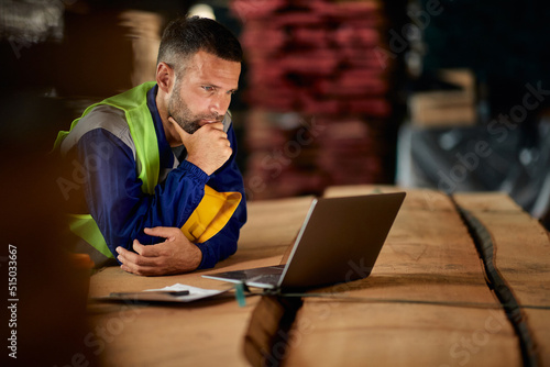 Slika na platnu Pensive foreman reading e-mail on laptop while working in warehouse