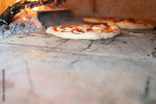 traditional neapolitan pizza coking in the wood fired oven with copy space, in the background flames and wood branding, pizza margherita with basil