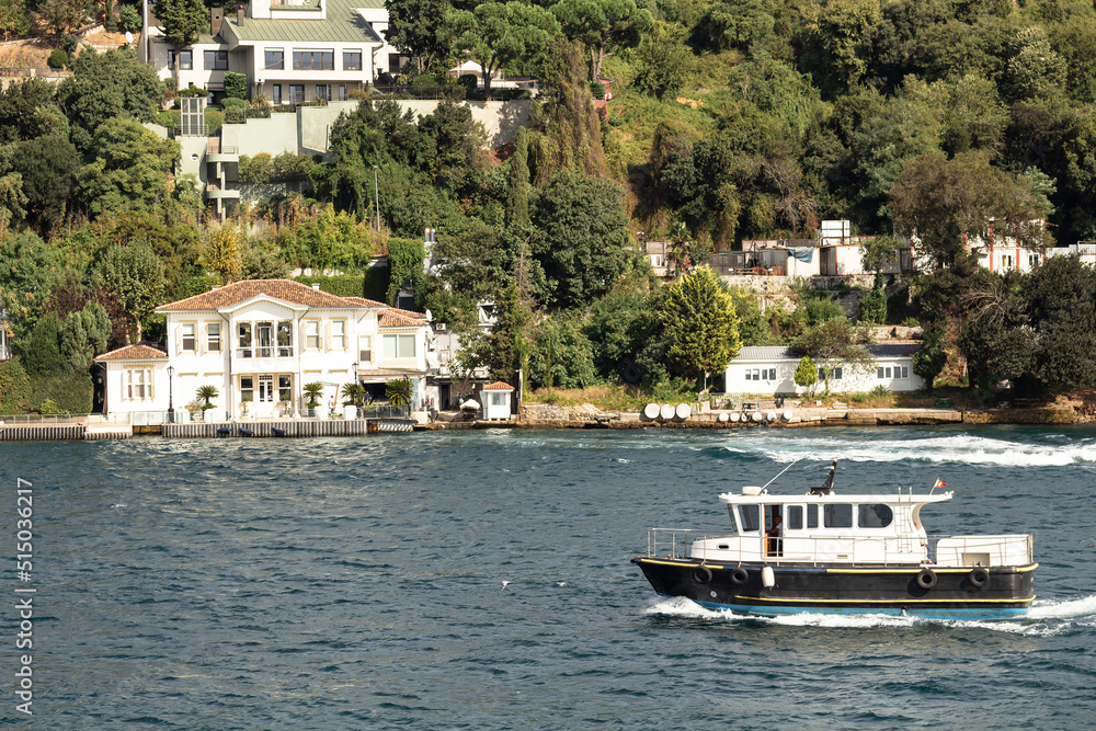 View of a fishing boat passing on Bosphorus by Anadolu Hisari neighborhood on Asian side of Istanbul. It is a sunny summer day. Beautiful travel scene.