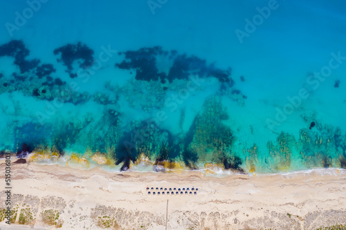 Umbrellas lined up on the sandy beach by the turquoise sea. Top view of a transparent blue sea with beautiful waves on the beach. Summer vibes concept. Exotic beach from above. Go Everywhere