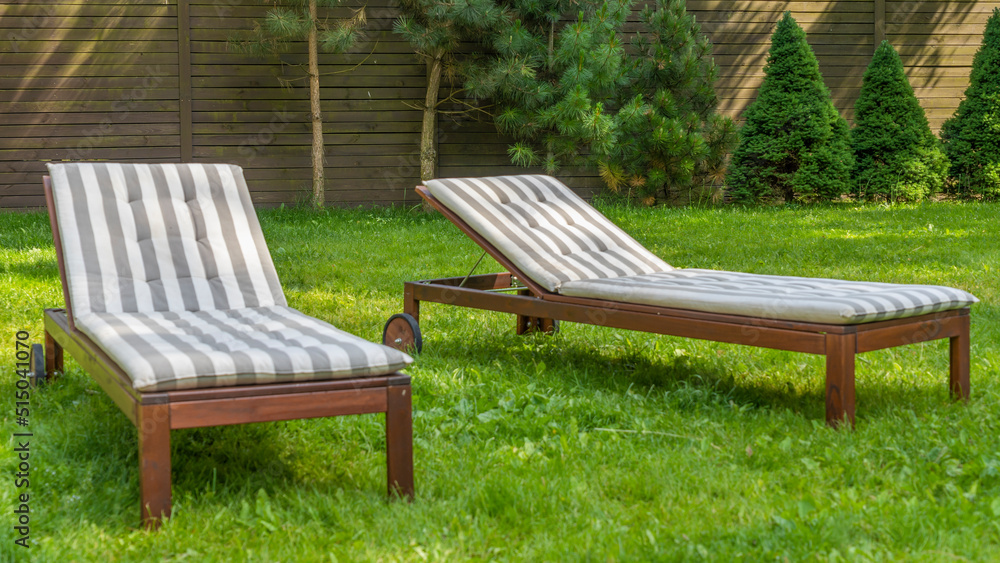 Lounge chairs on the backyard in a beautiful garden. Two empty sunbeds on the grass.