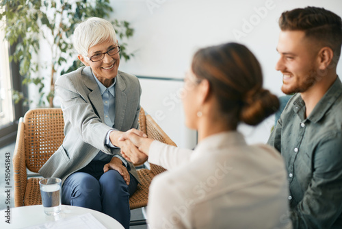 Happy senior financial advisor shaking hands with young couple on meeting in the office.