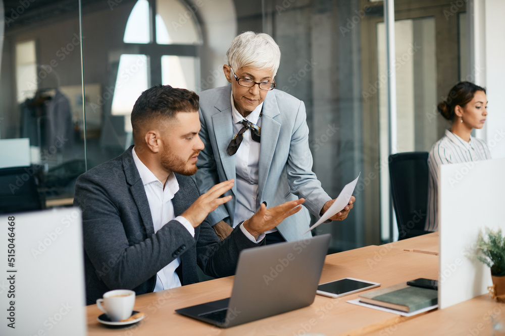 Mature businesswoman and her male colleague examining reports in office. Mature businesswoman and her male colleague examining reports in office.