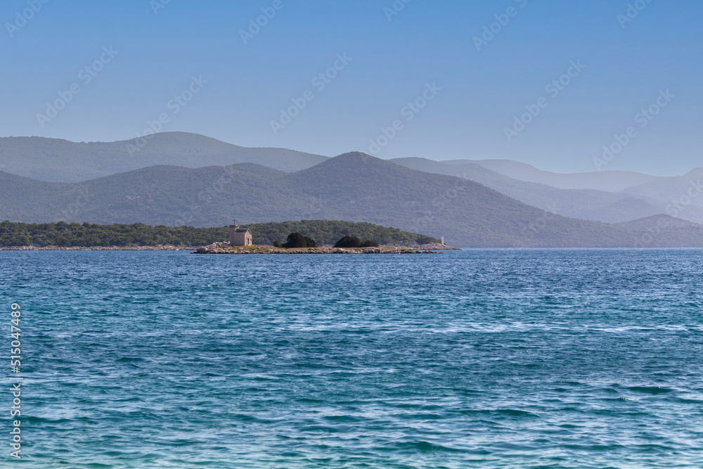 Coast in Croatia - pebble beach with beautiful blue sea in the background a small island with a church and beautiful mountains Coast in Croatia - pebble beach with beautiful blue sea in the background a small island with a church and beautiful mountains