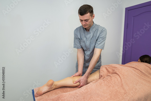 A male massage therapist massages the shin of a young woman