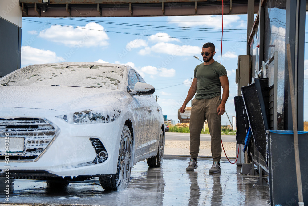 Man cleaning his car using high pressure water. Young man washing his
