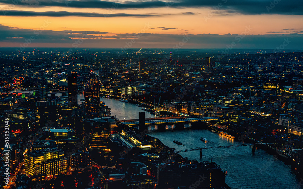 Aerial view of west London, blue hour just after sunset, orange yellow street lights starting to glow, river Thames separating two shores