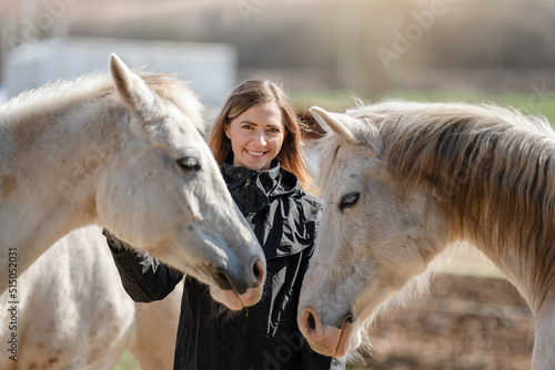 Young woman in black riding jacket standing near group of white Arabian horses smiling happy, one on each side, closeup detail