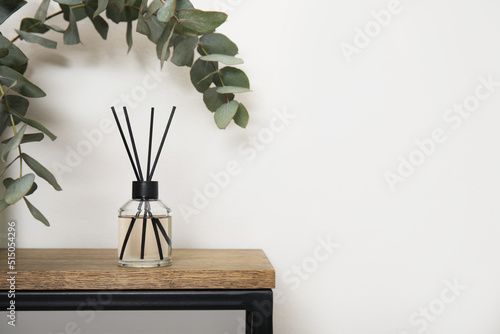 Photos Reed diffuser and eucalyptus on wooden table near white wall