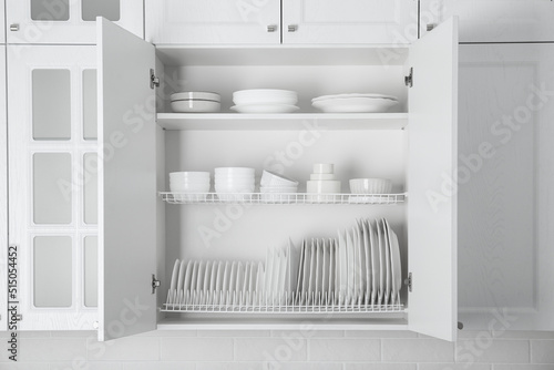 Open cabinet with different clean plates and bowls in kitchen