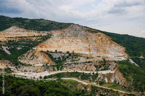 Natural quarry is located near road against backdrop of Rhodope Mountains and hills with forests and mountain vegetation