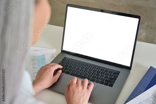 Female hands typing writing e mail letter using pc laptop computer with empty blank white screen for advertising at desk. Business technologies concept. Over shoulder view.