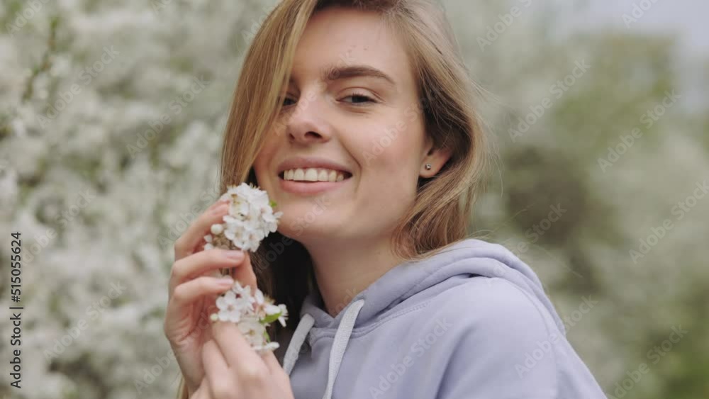 Smiling attractive woman posing with flowering cherry tree branch near her face outdoors. Portrait of positive young lady with blond hair among beautiful blooming park. Smiling attractive woman posing with flowering cherry tree branch near her face outdoors. Portrait of positive young lady with blond hair among beautiful blooming park.