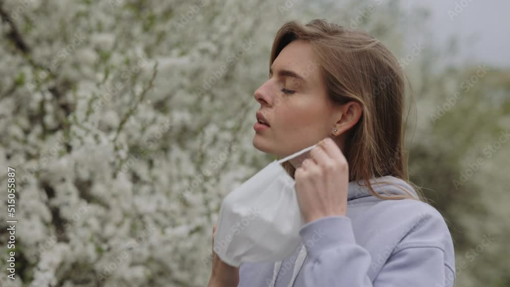 Delighted young woman feeling freedom after taking off her medical face mask. Charming caucasian blonde enjoying fresh air during warm spring day in blooming park. Delighted young woman feeling freedom after taking off her medical face mask. Charming caucasian blonde enjoying fresh air during warm spring day in blooming park.