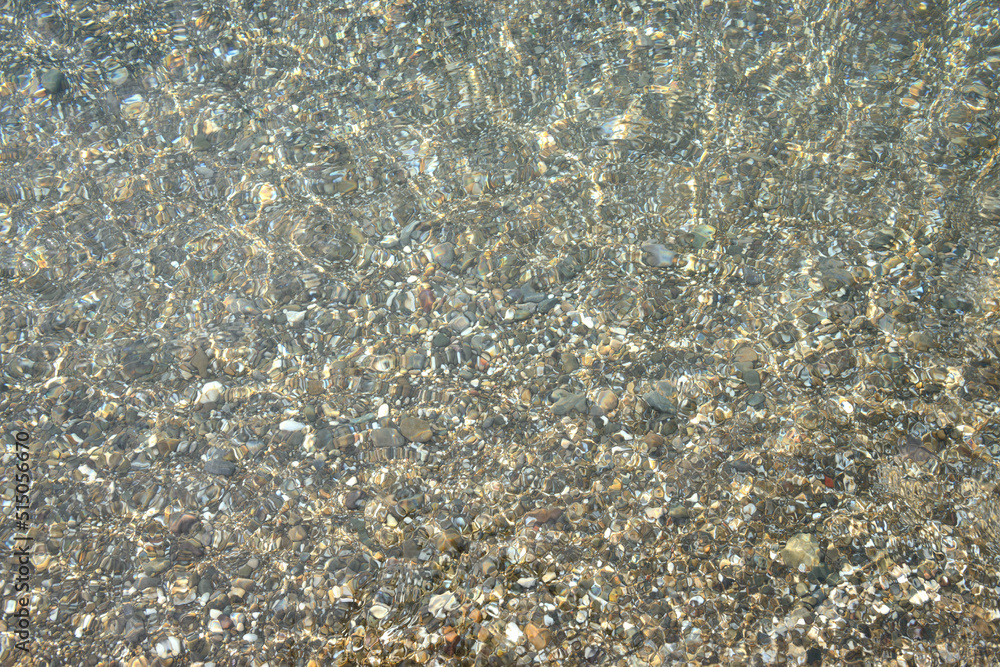 Shimmering sun glares on pebble seabed under water as background.