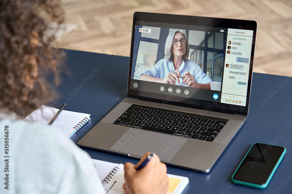 Girl student studying virtual course with remote teacher or tutor, learning distance class training, looking at laptop computer watching online webinar sitting at home table. Over shoulder screen view Girl student studying virtual course with remote teacher or tutor, learning distance class training, looking at laptop computer watching online webinar sitting at home table. Over shoulder screen view