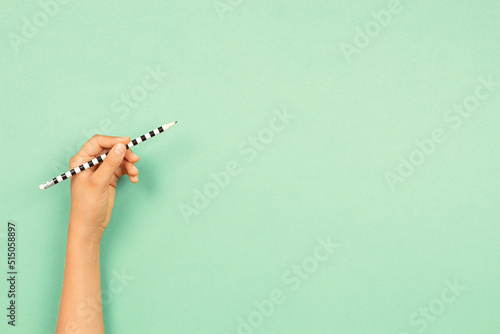 фотографія Left hand holding pencil for writing over light green background