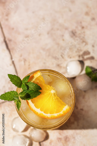 Summer iced cocktail with orange and mint on beige tile background with hard shadows. Top view, copy space