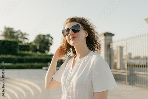 A woman with curly hair in sunglasses is posing in the park at the sunset. © Roman Tyukin