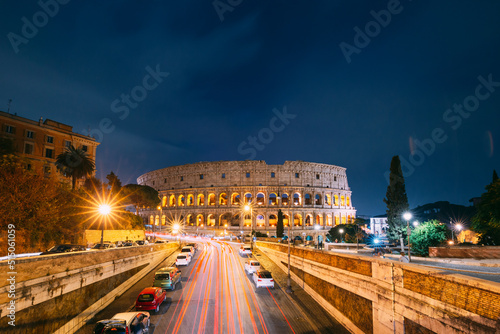 Rome, Italy. Colosseum Also Known As Flavian Amphitheatre In Evening Or Night Time. Night Traffic Light Trails Near Famous World Landmark.